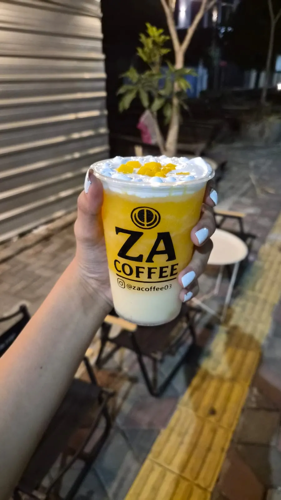 Es mangga dipegang di trotoar depan ZA Coffee, jalur pemandu kuning terlihat jelas di bawahnya