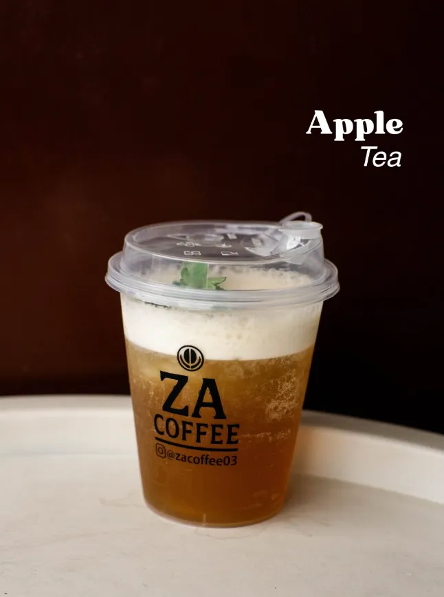 Segelas Apple Tea dengan busa di atasnya, latar cokelat gelap